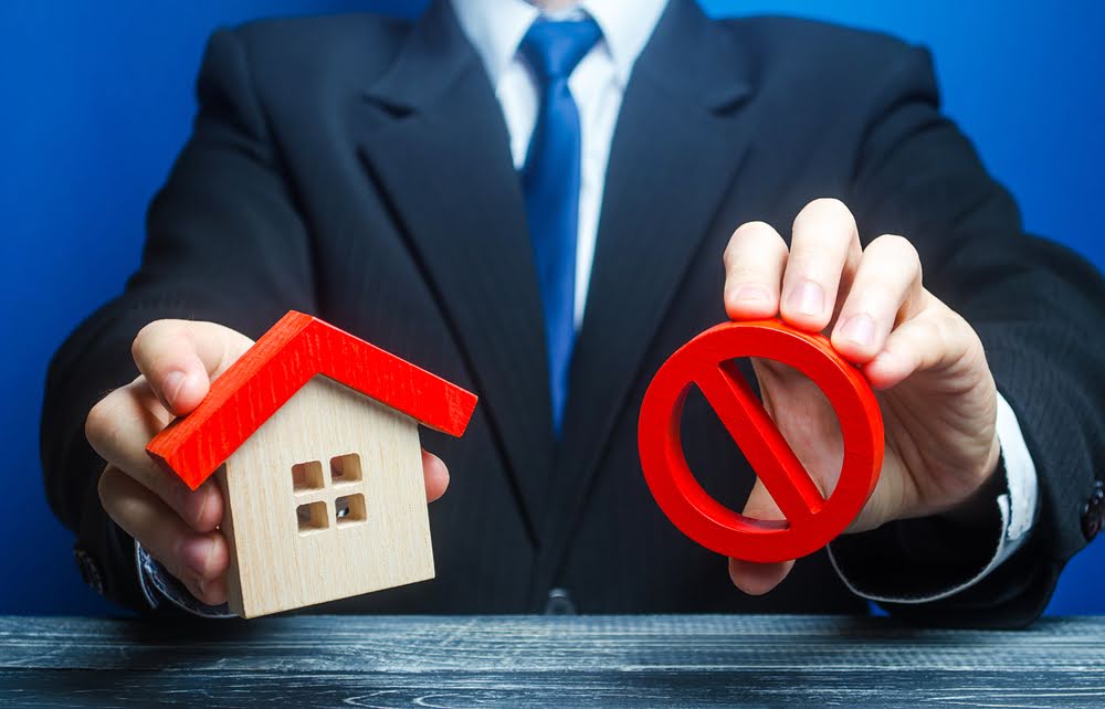 A man holds a house and the red prohibition symbol NO.